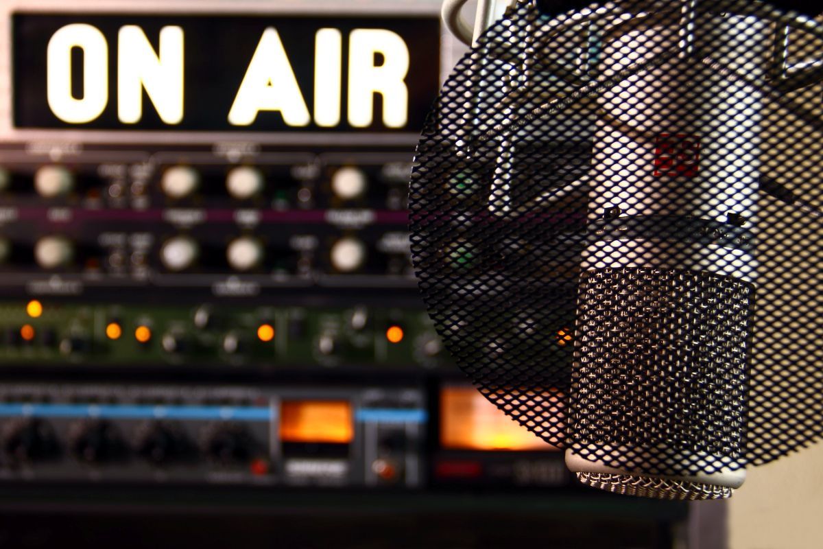 Ein Bild von einem Radio-Mikrofon im Vordergrund, im Hintergrund ist ein Leuchtschild, auf dem  "On Air" steht